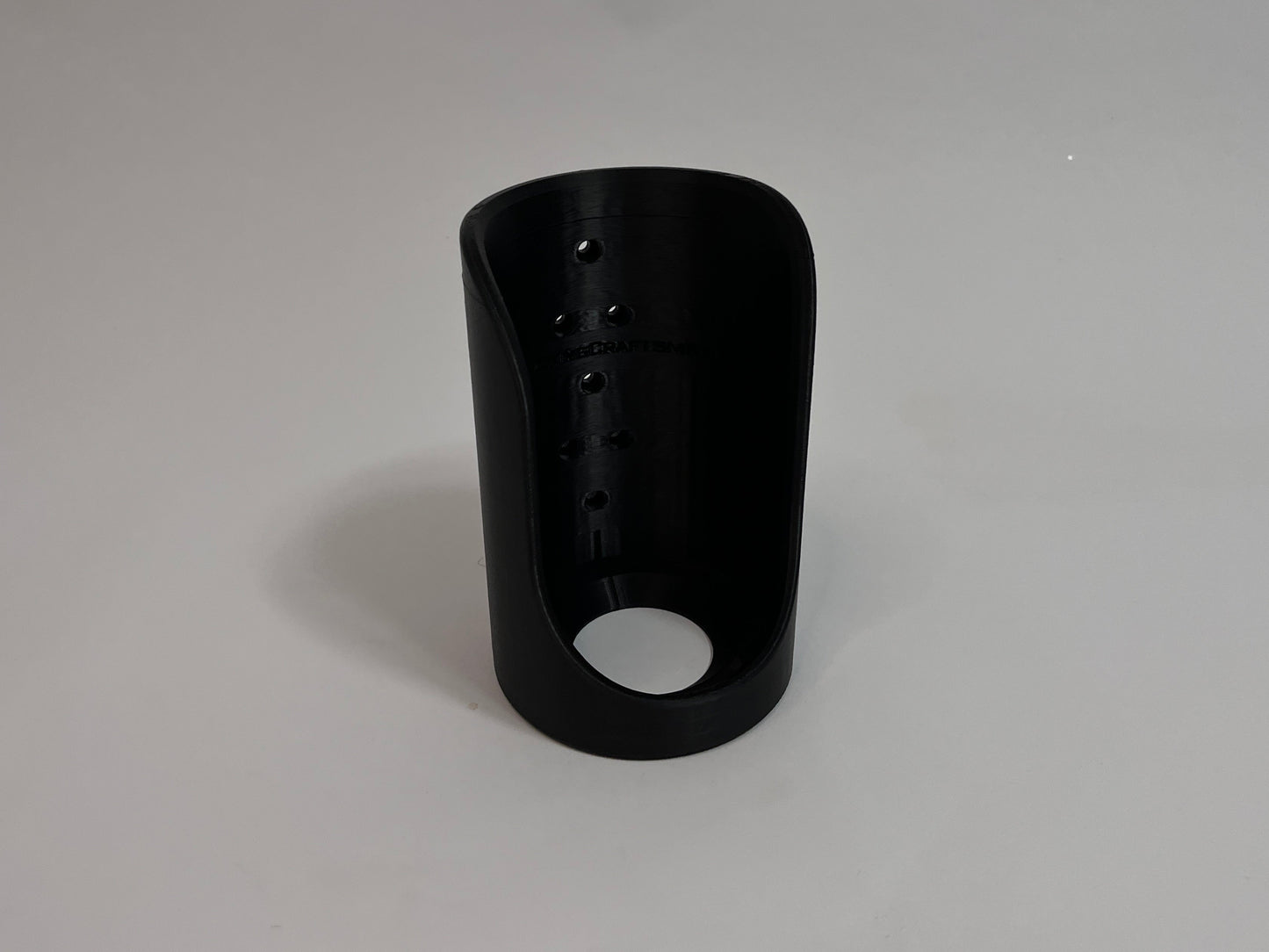 A black plastic cylindrical sleeve with a circular cutout at the bottom and a row of small ventilation holes on the side, shown on a neutral gray background.