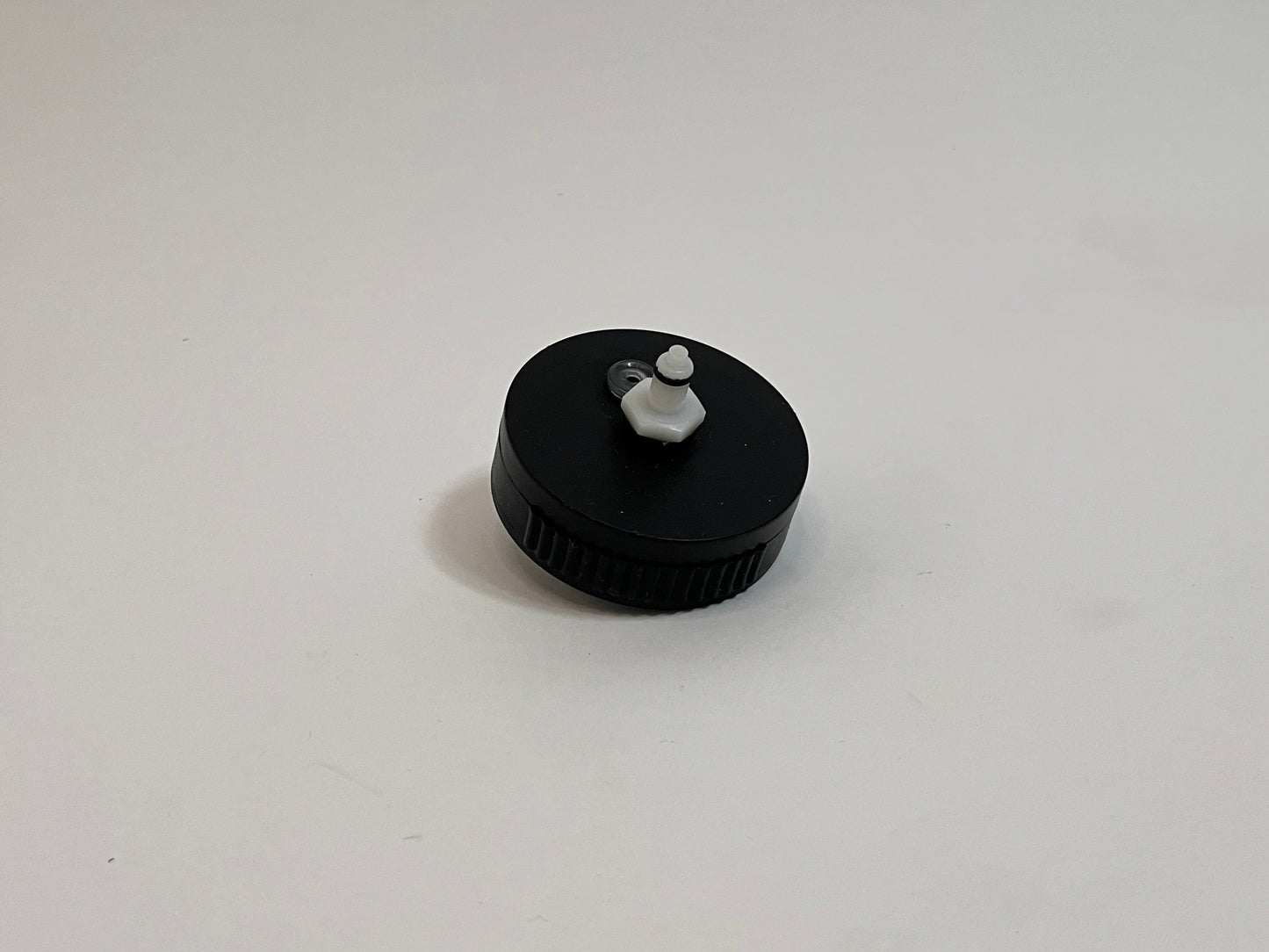 A small black plastic cap with a white plastic dry break water CPC fitting in the center, photographed on a plain light gray background.