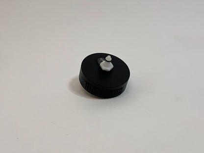 A small black plastic cap with a white plastic dry break water CPC fitting in the center, photographed on a plain light gray background.