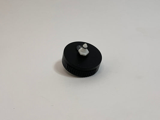 A small black plastic cap with a white plastic dry break water CPC fitting in the center, photographed on a plain light gray background.