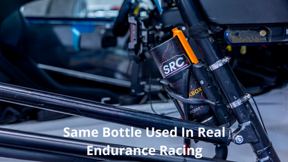 A close-up of a black endurance racing bottle holder mounted on a roll cage, holding a black bottle with an orange cap. The image features a text overlay reading 'Same Bottle Used In Real Endurance Racing' and is set against the blurred background of a race car interior.