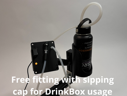 A black insulated bottle with a white sipping tube connected to a DrinkBox and black mounting bracket, shown against a light gray background with overlaid text reading 'Free fitting with sipping cap for DrinkBox usage.'.