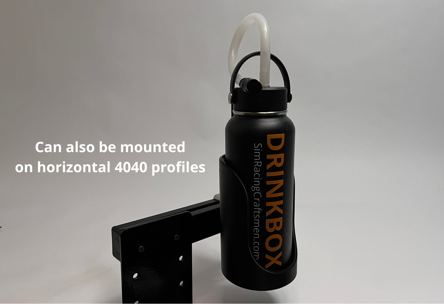 A black Drinkbox insulated water bottle with a white straw, shown mounted on a black metal bracket. White text on the left reads 'Can also be mounted on horizontal 4040 profiles'.
